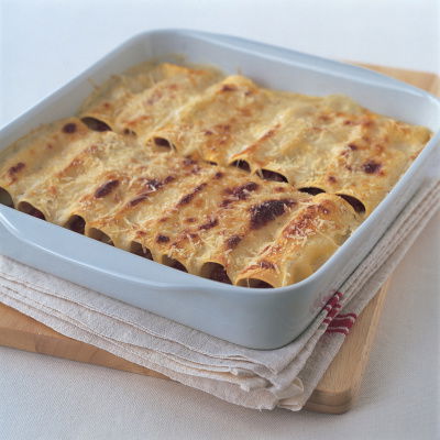 A square white dish with pasta sheets filled and rolled with the ragu sauce and parmesan cheese grated on the top