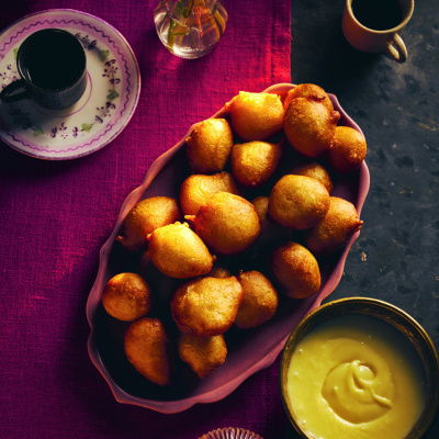 A picture of a table with a purple cloth and an oval bow of puff puffs with a little round dish and a candle on the side