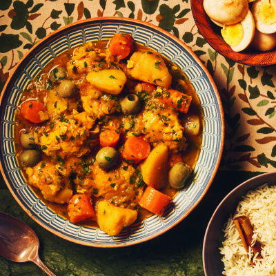 A picture of a table set with a colourful table cloth and bowls of tagine, rice and eggs 