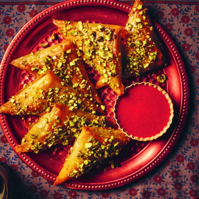 A picture of a red plate with samsas and a little bowl of strawberry coulis on the side