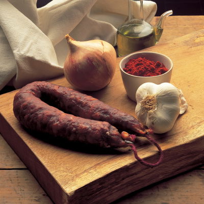 Onion, garlic, chorizo sausage and a cup full of paprika sat on a wooden chopping board