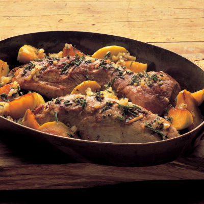 an oval casserole dish of roast pork, with apples on a wooden board