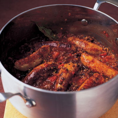 a pan of cooked sausages and puy lentils on a wooden board