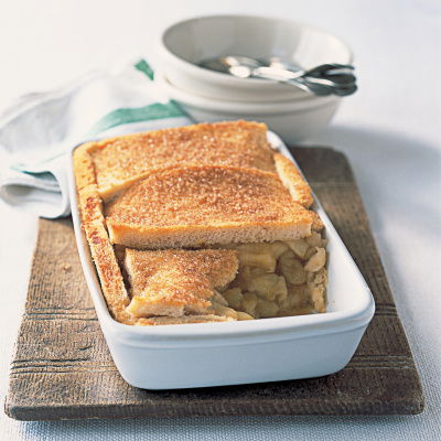 An oblong white dish with apple and orange filling and a layer of thin slices of bread to make the crunch topping