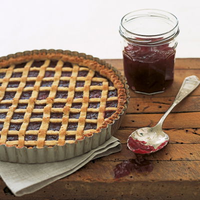 a picture of a linzertorte tarte in a flan tin with latticed pastry across the top and a jar of jam and spoon next to it
