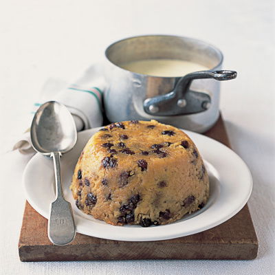 A picture of the pudding turned out on to a white dish with a serving spoon resting on the side and a pan of sauce in the background