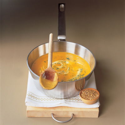 a saucepan filled with soup sitting on a white tablecloth with a wooden spoon resting on the pan