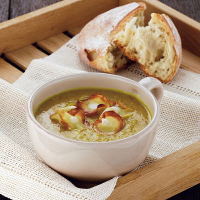 A bowl of parsnip soup in a white mug, with parsnip crisps on the top, sittin on a wooden tray with a roll of white bread next to it