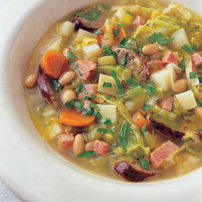 A white bowl of soup showing diced vegetables and frankfurter