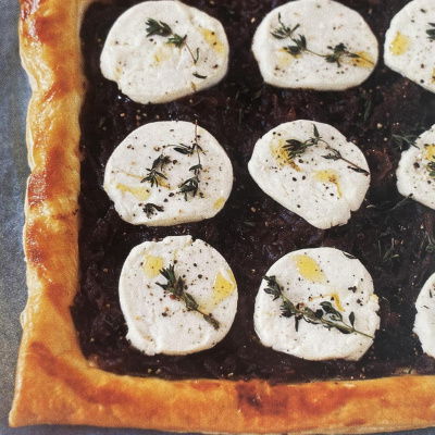 A sheet of cooked puff pastry with a layer of red onion and nine rounds of goats' cheese and some fresh thyme and oil drizzled over the top