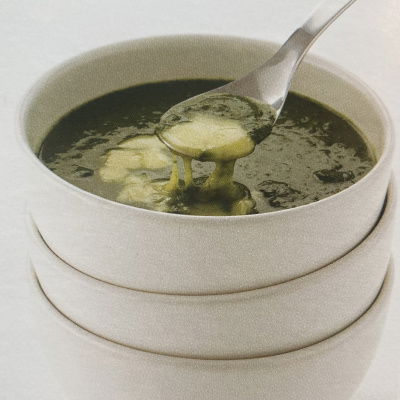 a picture of spinach soup and melted cheese in a white soup bowl with spoon