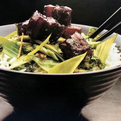 Cooked pork and stirefry greens in a brown bowl with two chopsticks resting on the side