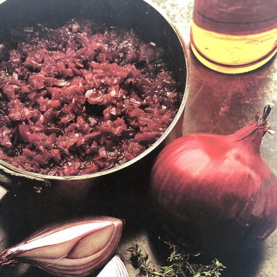 a pan of red onion marmalade with a whole red onion and a quartered red onion and a bunch of thyme on the side