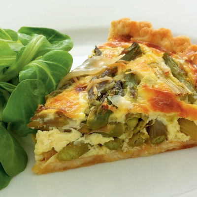 a picture of a slice of asparagus tart with salad leaves on a white plate