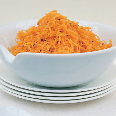 Grated carrot in a white bowl on top of a stack of four white plates