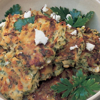 A white bowl of cooked potato cakes with feta cheese and parsley scattered on top