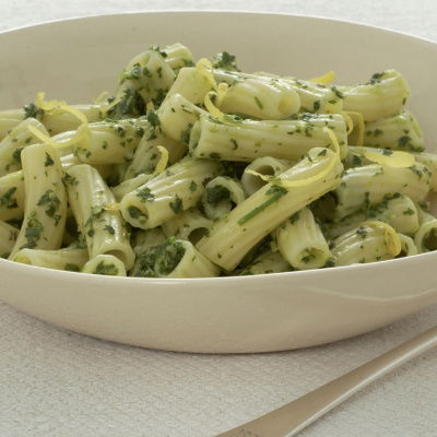 A white bowl of cooked pasta with flecks of herbs and lemon zest