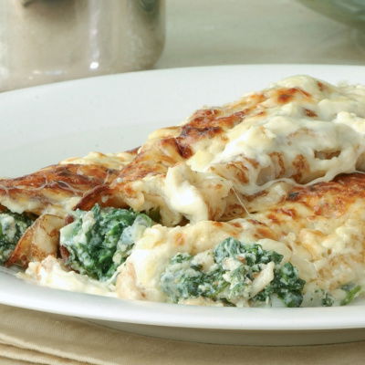 A picture of cooked pancake cannelloni on a white plate with spinach and a cheese sauce