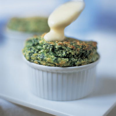 a ramekin with cooked spinach souffle and a spoon dripping sauce on top