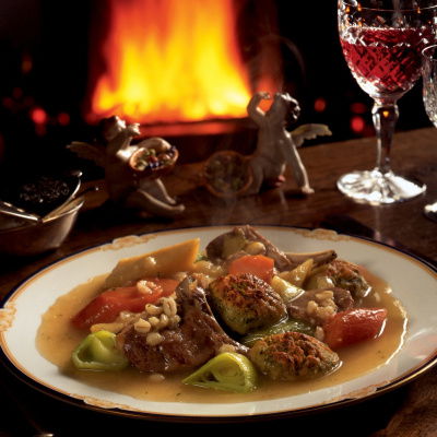 a picture of a table set with a plate of irish stew and a glass of wine witih a fire glowing in the background