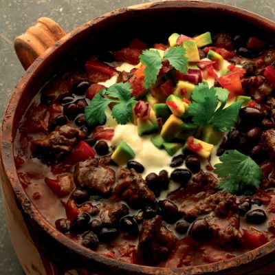 An earthenware bowl containing chilli beef with creme fraiche and avocado salsa on the top and a little parsley garnish