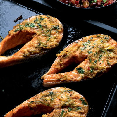 three cooked salmon steaks on a black roasting tin, with a bowl of salsa on the side